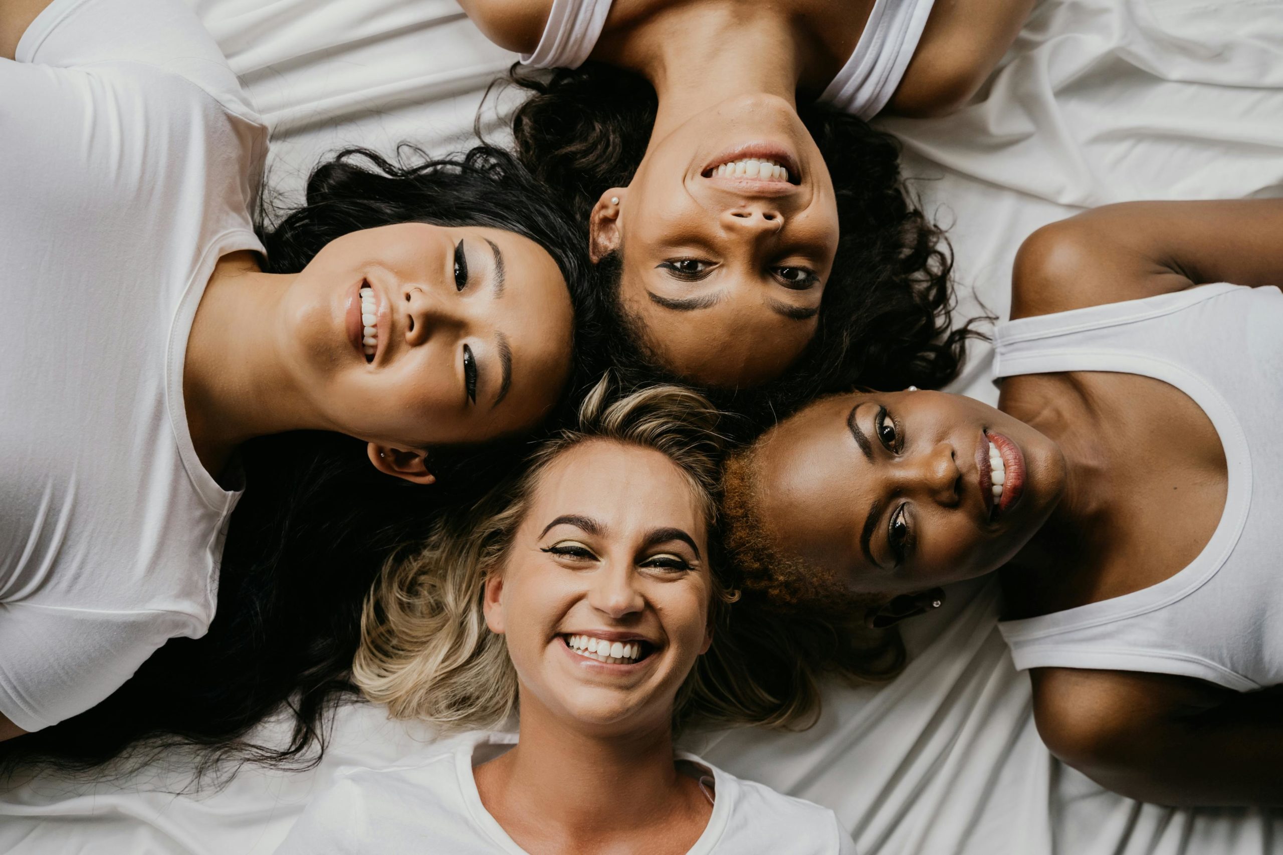 4 femmes en cercle et leur tête se touche en regardant vers le plafond